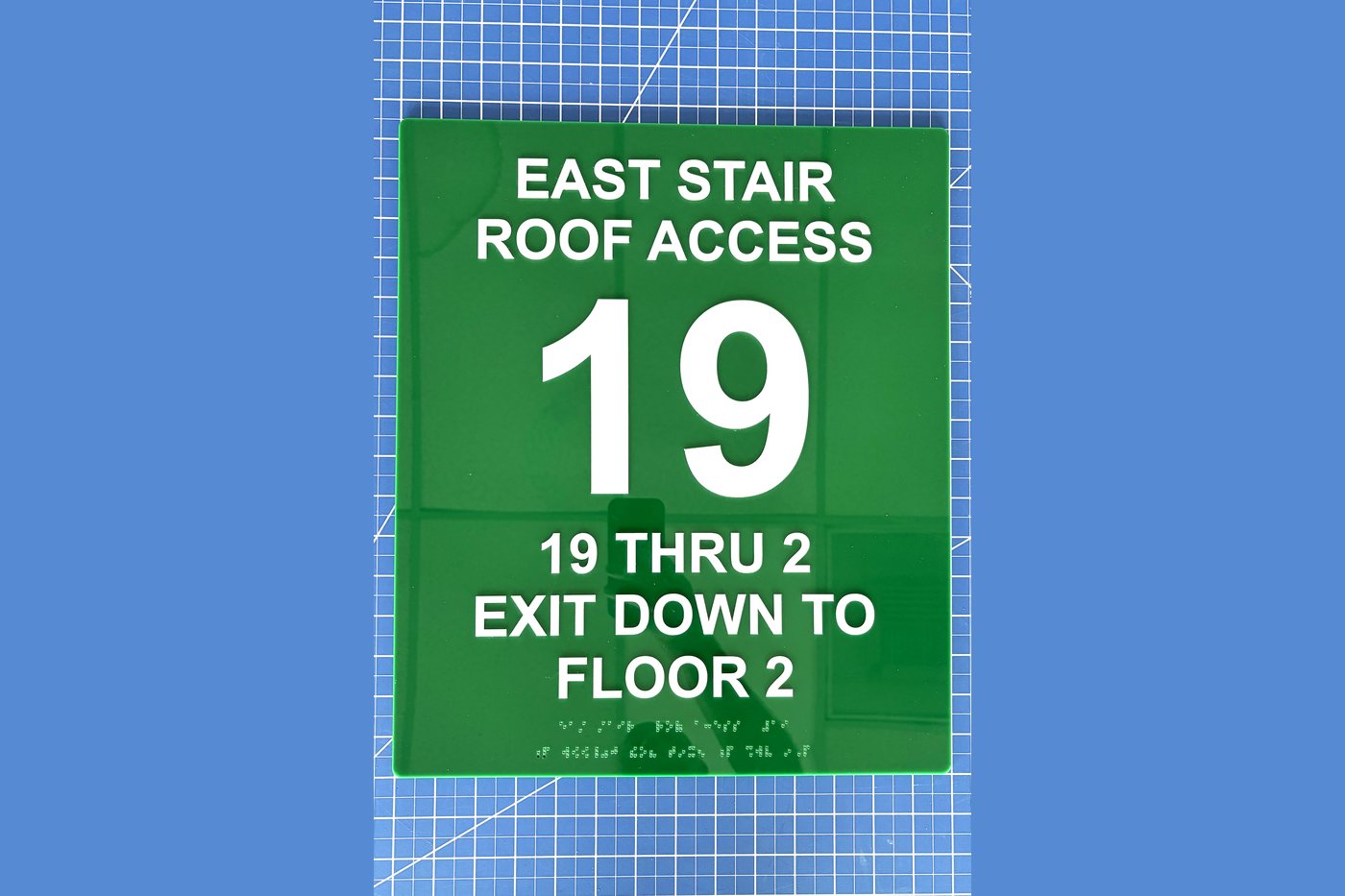Green stair identification sign reading East Stair Roof Access, floor 19, exit down to floor 2, with Braille
