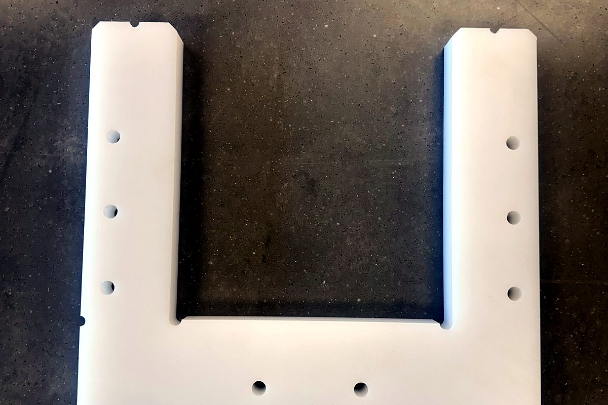 CNC-routed white poly machine bracket with drilled and countersunk holes