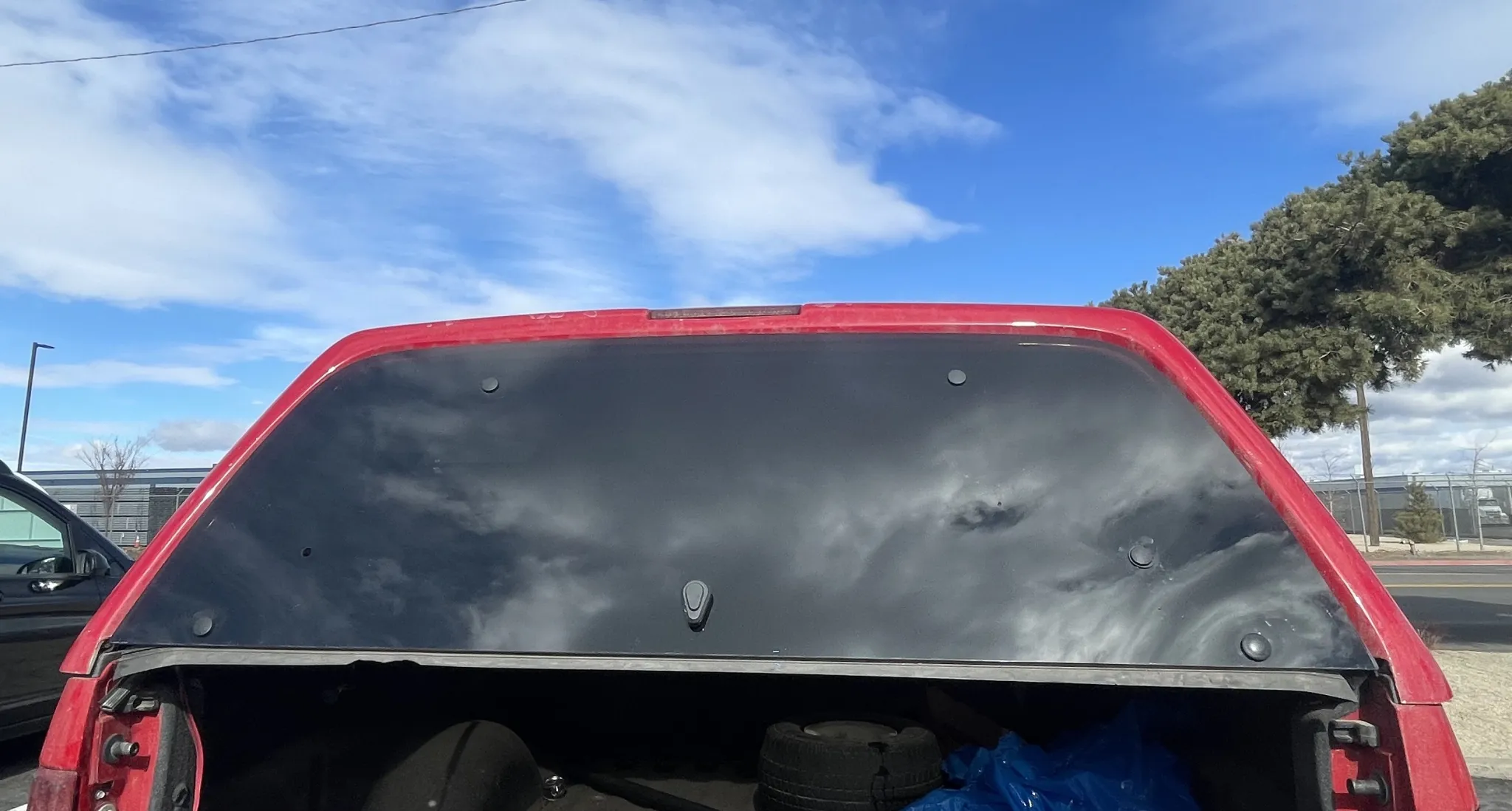 Open tailgate of red pickup truck under blue sky.