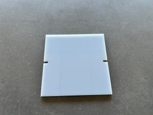 Square white plastic tile on gray surface.