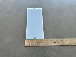 A ruler measuring a white plastic piece.